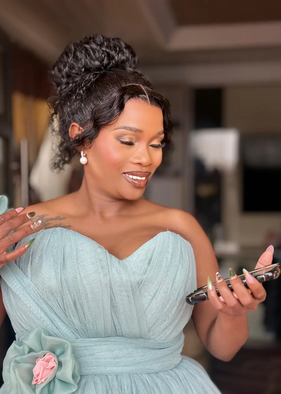 Woman in a mint dress wearing a curly high-bun updo with face-framing tendrils