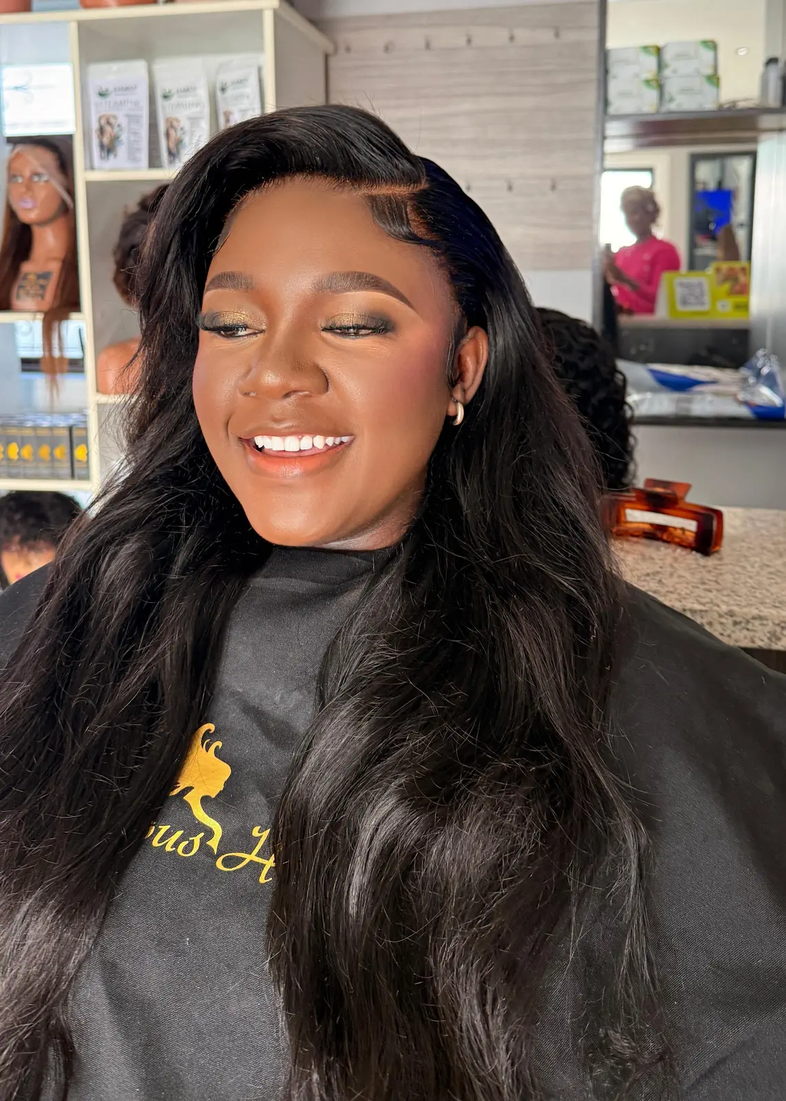 Smiling woman wearing long, side-parted black hair with soft waves at Licious Hair salon