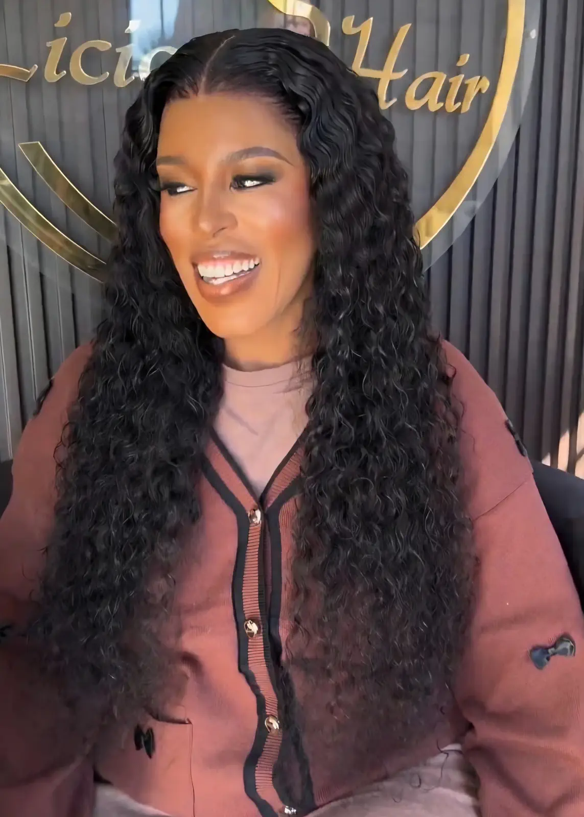 Smiling woman wearing long, centre-parted black hair with defined waves at Licious Hair salon