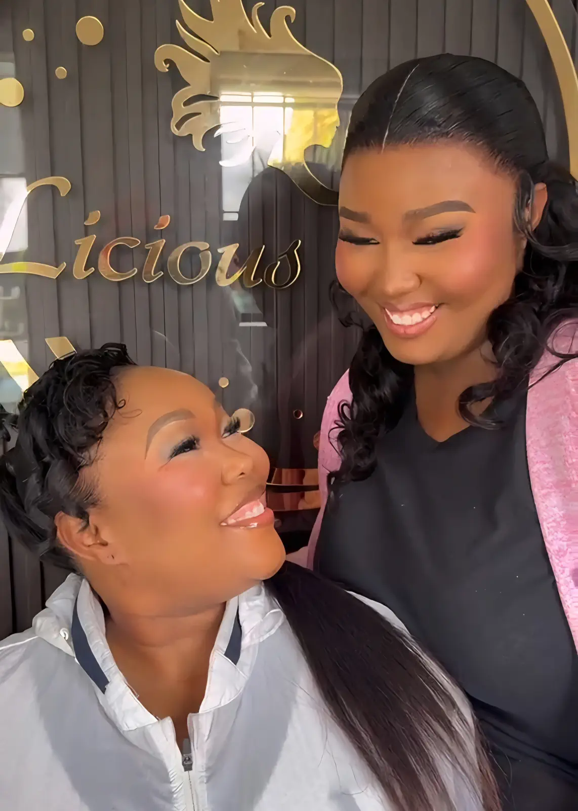 Two smiling women showing a sleek long ponytail and curled black hairstyle at Licious Hair salon