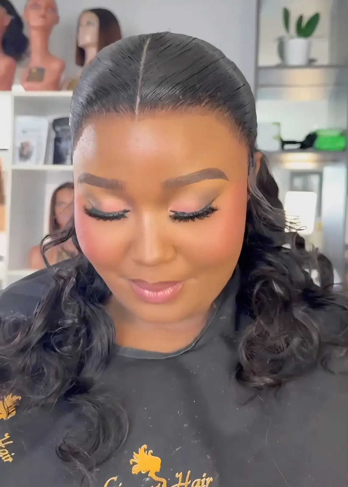 Woman with centre-parted black hair styled into a low ponytail with soft curls at Licious Hair salon
