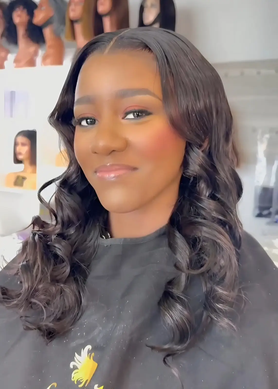 Woman wearing long, side-parted black hair styled in loose curls at Licious Hair salon