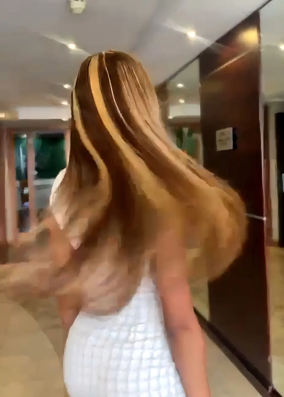 Back view of a woman swishing long, straight honey-blonde highlighted hair